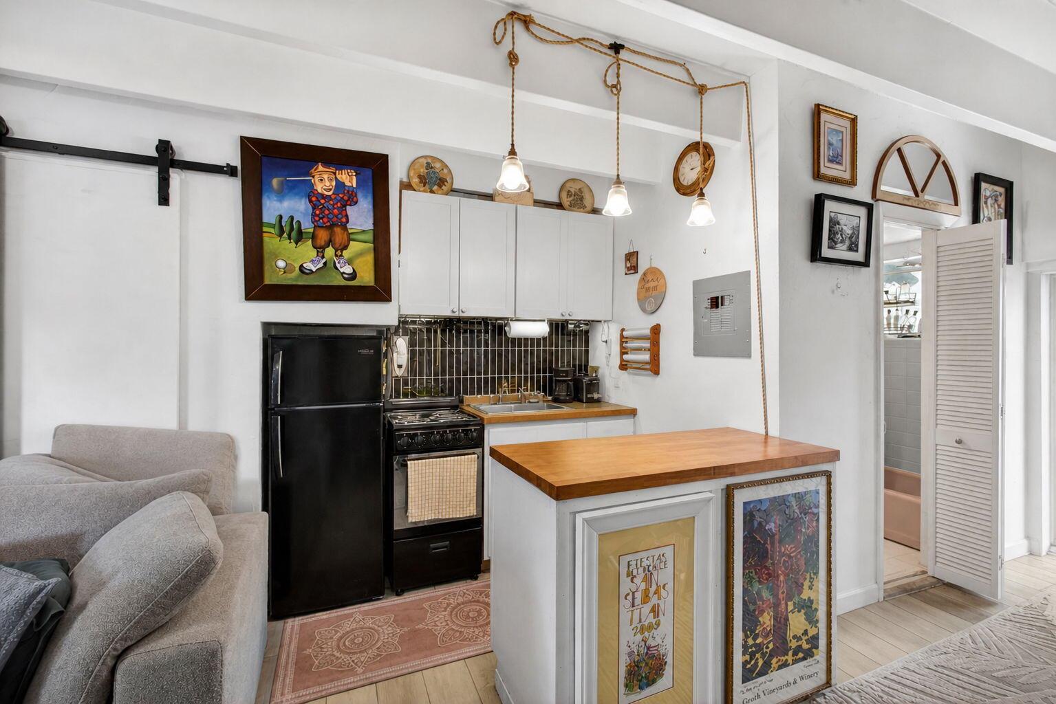 A small kitchen features white cabinets, a black stove and refrigerator, and a wooden island — 4001 S Ocean Boulevard # 111, Palm Beach FL 33480, PALM BEACH, FL