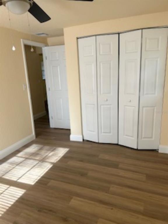 A room with light-colored walls, wood-look flooring, a ceiling fan, and white bi-fold closet doors — 26356 ROLLING ACRES DRIVE, BROOKSVILLE, FL