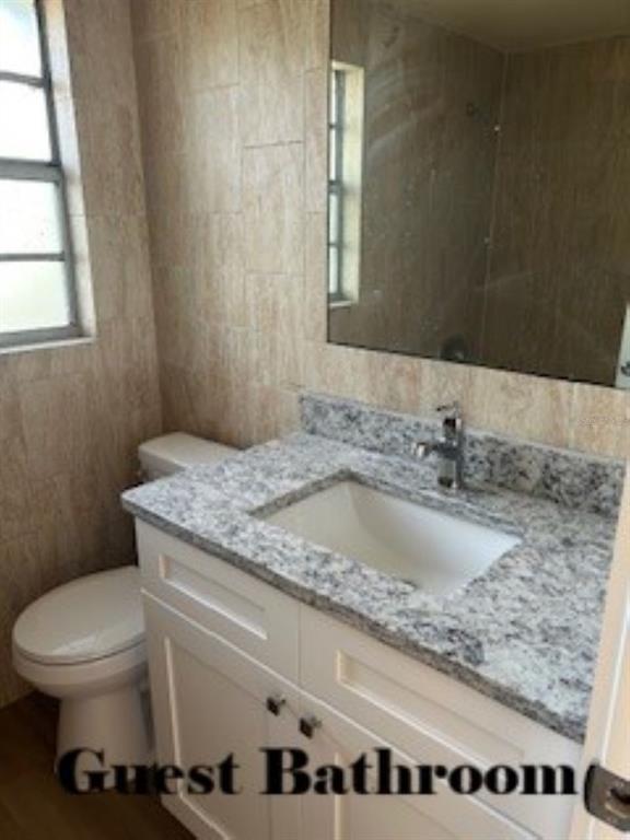 A guest bathroom features a white vanity with a granite countertop and a wall-mounted mirror — 26356 ROLLING ACRES DRIVE, BROOKSVILLE, FL