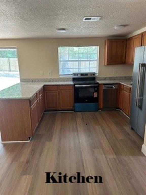 A kitchen features wood cabinets, granite countertops, stainless steel appliances, and light wood-look flooring — 26356 ROLLING ACRES DRIVE, BROOKSVILLE, FL