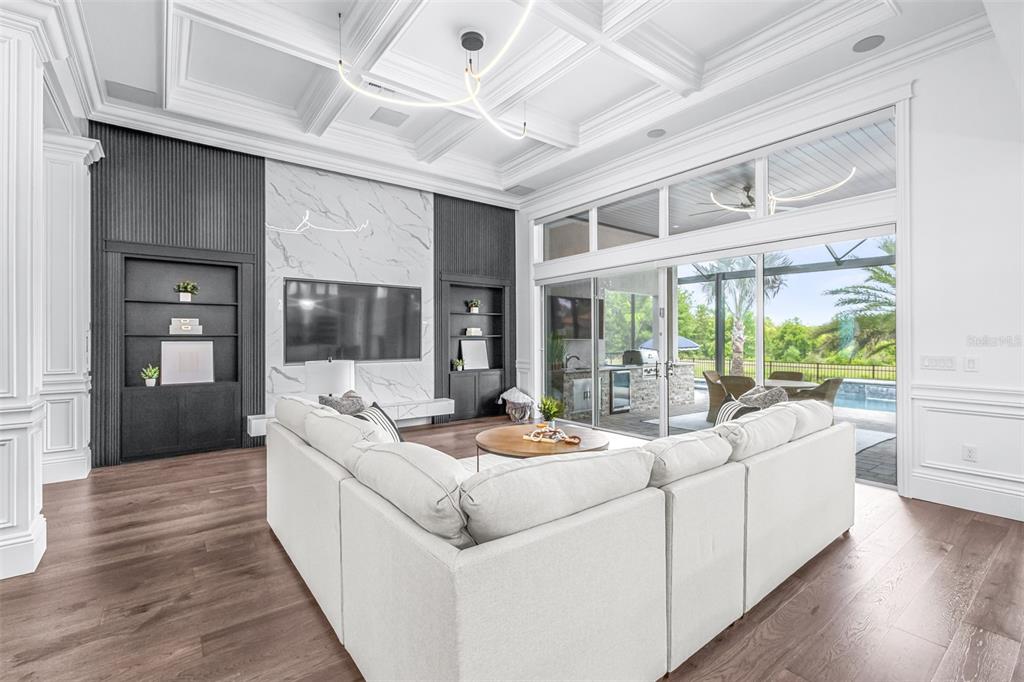 A modern living room features a white sectional sofa, marble fireplace wall, and large sliding doors — 7190 GRAYBROOK DRIVE, WESLEY CHAPEL, FL