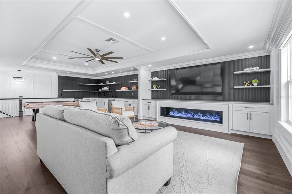 A modern living room features a fireplace, built-in shelving, a sofa, and a game table — 7190 GRAYBROOK DRIVE, WESLEY CHAPEL, FL