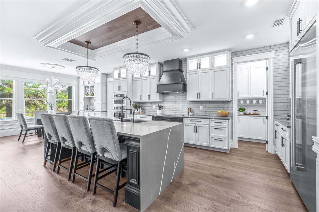 A modern kitchen features a large gray stone island, white cabinetry, and two crystal chandeliers — 7190 GRAYBROOK DRIVE, WESLEY CHAPEL, FL