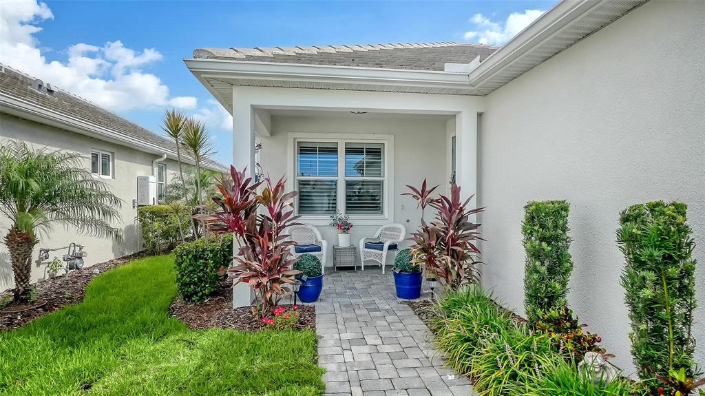 A paved walkway leads to a covered front porch with two chairs and potted plants — 8152 STERNWAY ROAD, SARASOTA, FL