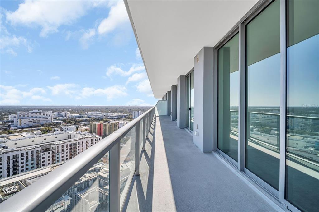 A long, narrow balcony with glass railings overlooks a city skyline under a blue sky — 400 CENTRAL AVENUE UNIT 2205, ST PETERSBURG, FL