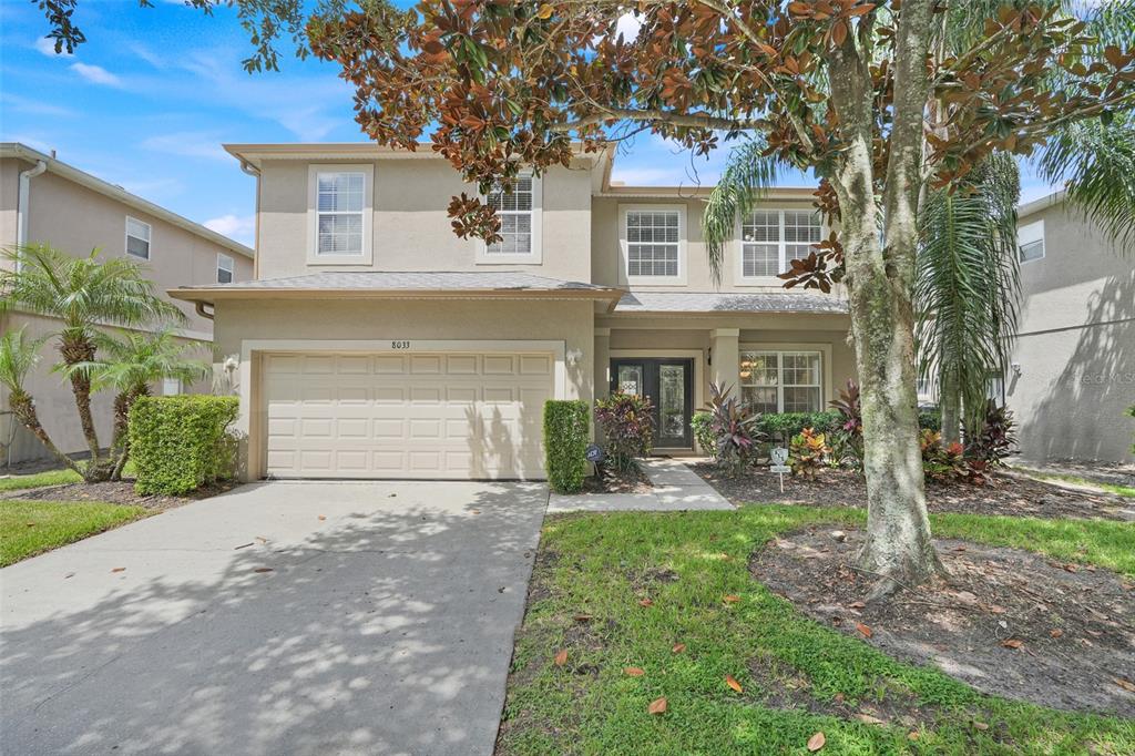 A two-story suburban house with a beige stucco exterior, a two-car garage, and landscaping — 8033 ACADIA ESTATES COURT, KISSIMMEE, FL