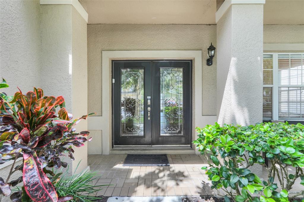 A front entryway features double glass-paneled doors, a tiled porch, and surrounding landscaping — 8033 ACADIA ESTATES COURT, KISSIMMEE, FL