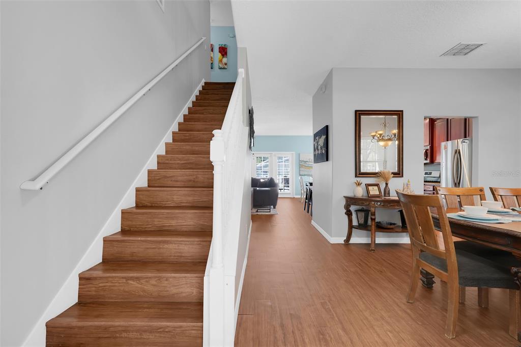 A staircase with wood treads leads upward next to a dining area and living room — 8033 ACADIA ESTATES COURT, KISSIMMEE, FL