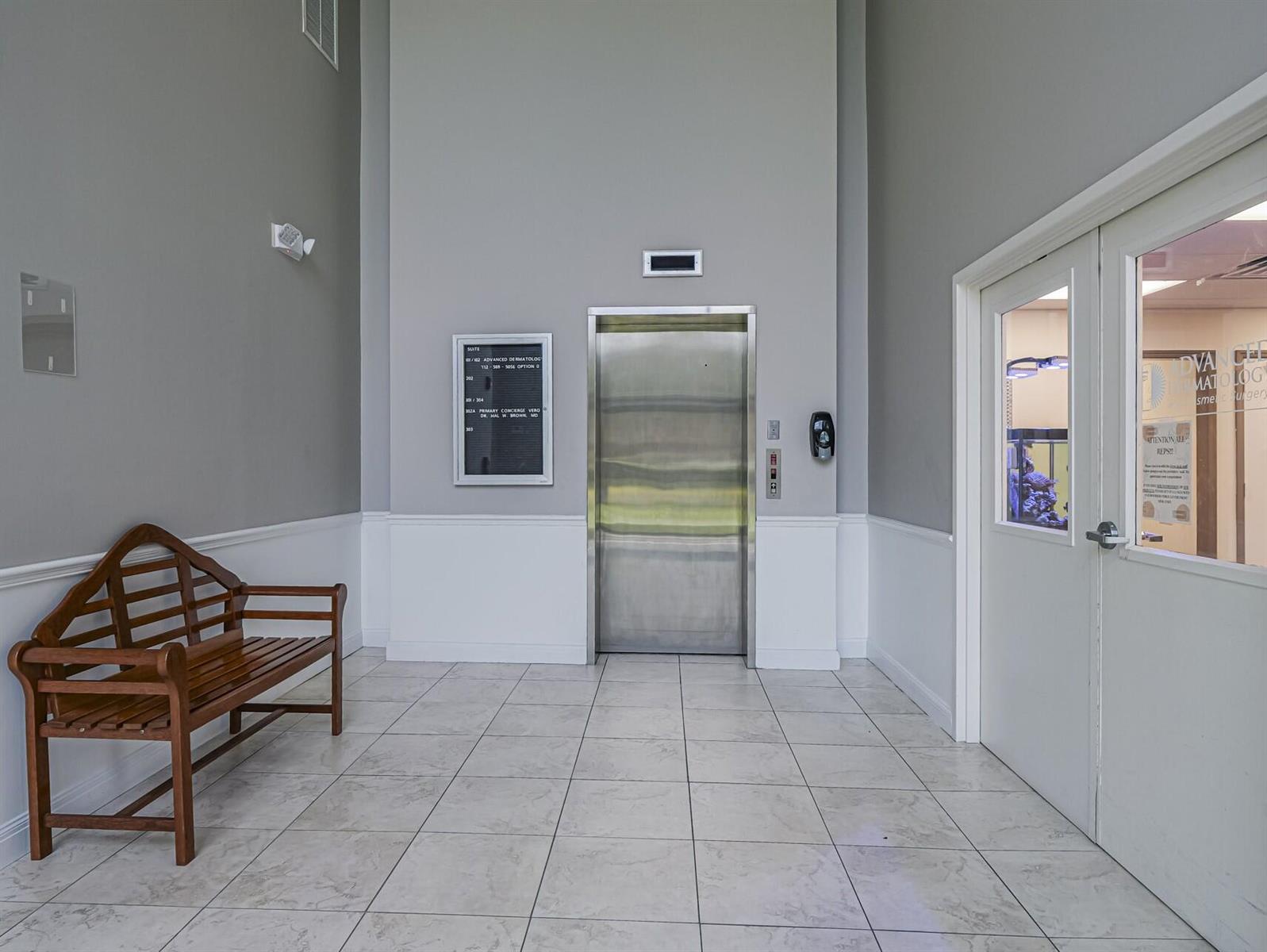 A waiting area features a wooden bench, a stainless steel elevator, and a glass-paneled door — 3755 7th Terrace # B, Vero Beach FL 32960, VERO BEACH, FL