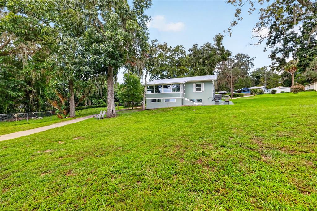 A light green house sits on a grassy hill surrounded by large, moss-covered trees — 13462 SE 108TH COURT ROAD, OCKLAWAHA, FL