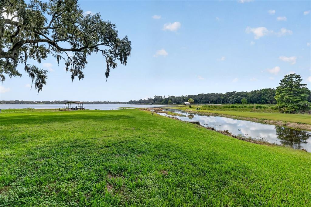 A grassy lawn leads to a narrow canal and a large lake with a dock — 13462 SE 108TH COURT ROAD, OCKLAWAHA, FL