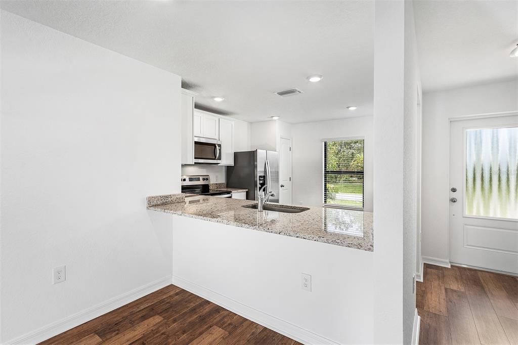 A kitchen with granite countertops and white cabinets overlooks a dining area with wood flooring — 5952 GILLOT BOULEVARD, PORT CHARLOTTE, FL