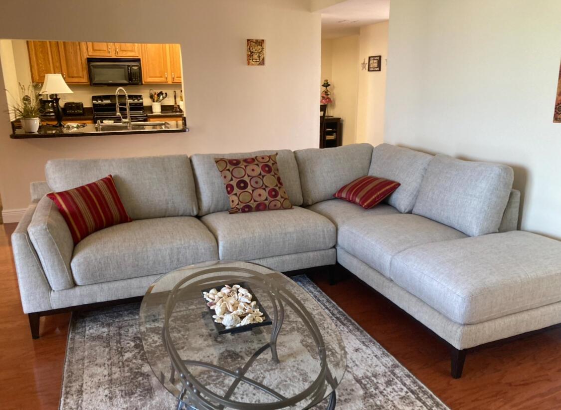 A living room features a light gray sectional sofa, a glass coffee table, and a kitchen pass-through — 2255 Lindell Boulevard # 4404, Delray Beach FL 33444, DELRAY BEACH, FL