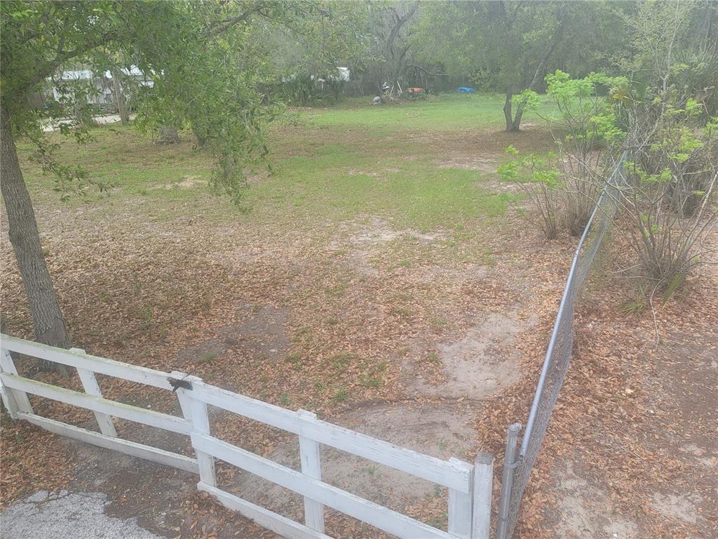 A grassy, partially shaded lot is enclosed by a white wooden fence and chain-link fencing — 11641 BRUIN DRIVE, NEW PORT RICHEY, FL