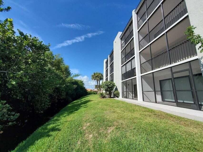 A multi-story apartment building with screened balconies overlooks a grassy lawn and dense trees — 1605 S Us Highway 1 # F203, Jupiter FL 33477, JUPITER, FL