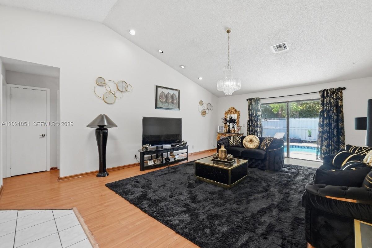 A living room features a vaulted ceiling, black furniture, a large rug, and sliding glass doors — 4080 NW 1st Pl, Deerfield Beach FL 33442, DEERFIELD BEACH, FL