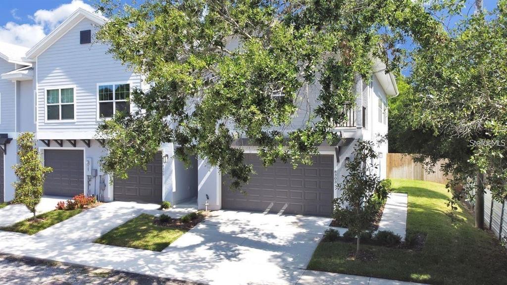A two-story townhouse with light blue siding, two garage doors, and a large tree in front — 8303 KING BLOSSOM COURT, TAMPA, FL