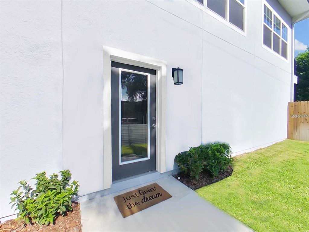 A gray door with a glass panel and a welcome mat sits on a concrete walkway — 8303 KING BLOSSOM COURT, TAMPA, FL