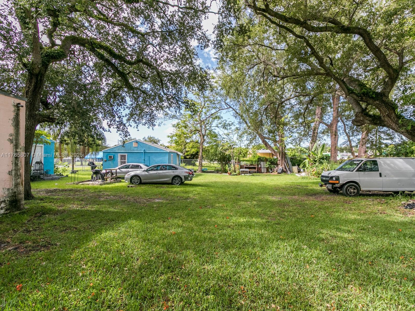 A large, grassy backyard features several parked vehicles, mature trees, and a blue house — 7946 NW 12th Pl, Miami FL 33147, MIAMI, FL