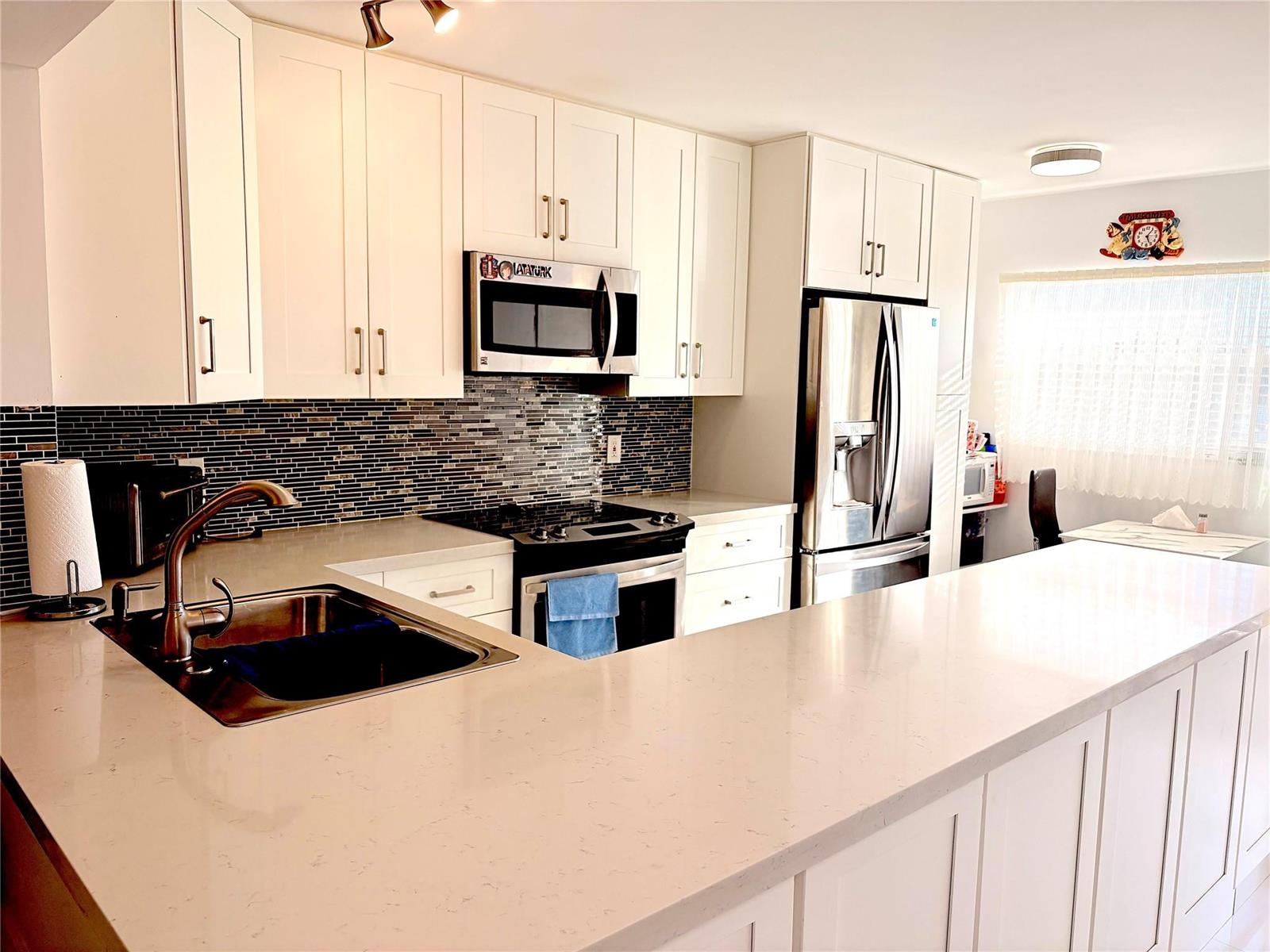 A kitchen features white cabinetry, stainless steel appliances, a quartz countertop, and a tiled backsplash — 23099 Barwood Lane # 308, Boca Raton FL 33428, BOCA RATON, FL