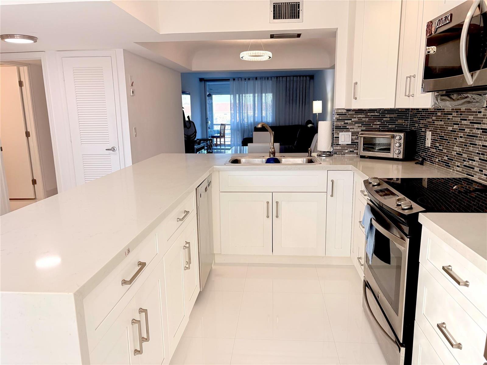 A modern kitchen features white cabinets, quartz countertops, stainless steel appliances, and a tiled backsplash — 23099 Barwood Lane # 308, Boca Raton FL 33428, BOCA RATON, FL