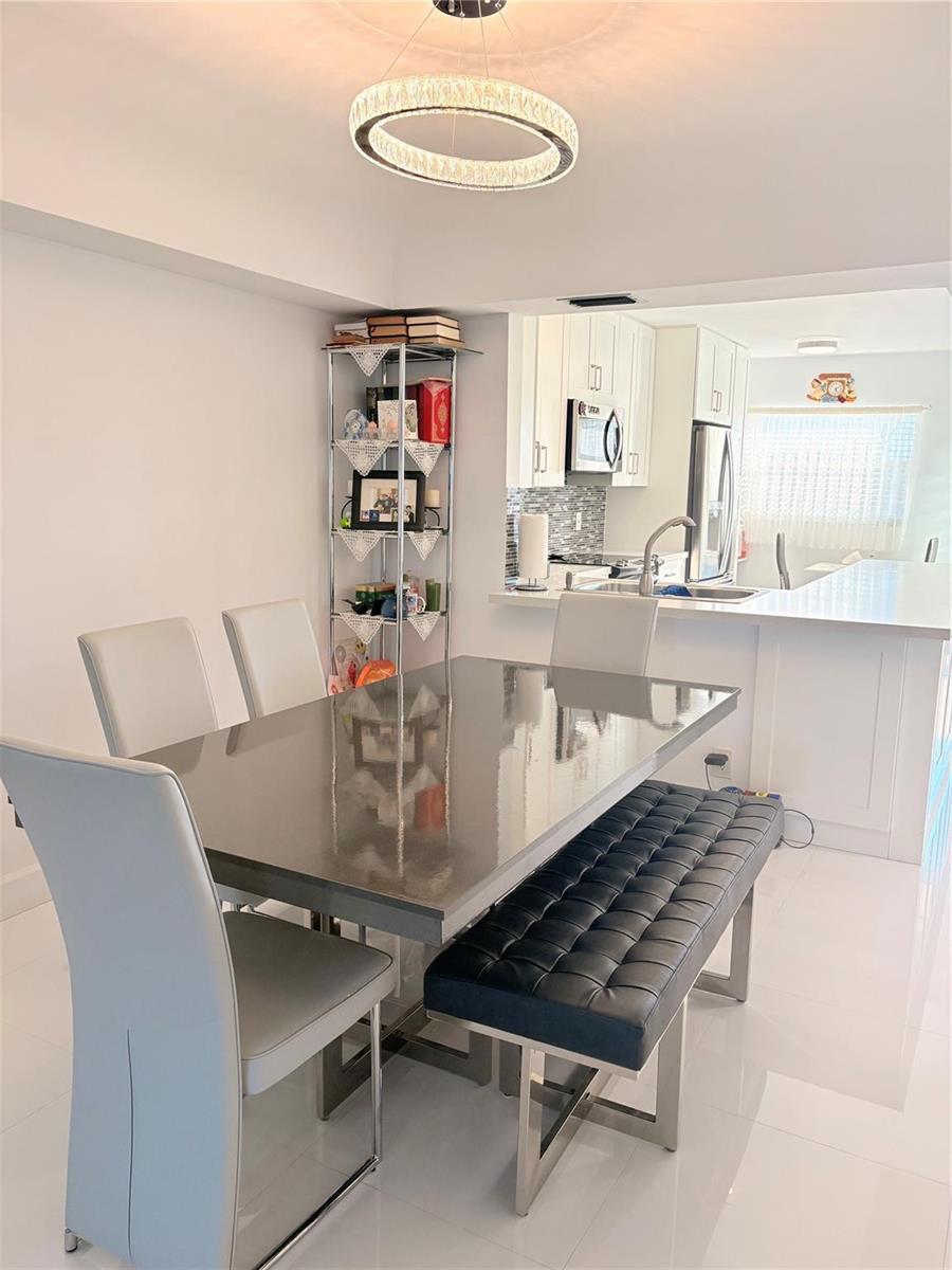 A dining area with a gray table, chairs, and a tufted bench near a kitchen — 23099 Barwood Lane # 308, Boca Raton FL 33428, BOCA RATON, FL