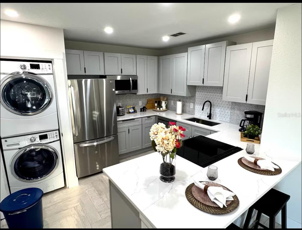 A kitchen and dining area featuring light wood-look flooring, white cabinetry, and a stacked laundry unit — 1756 2ND STREET NE, WINTER HAVEN, FL