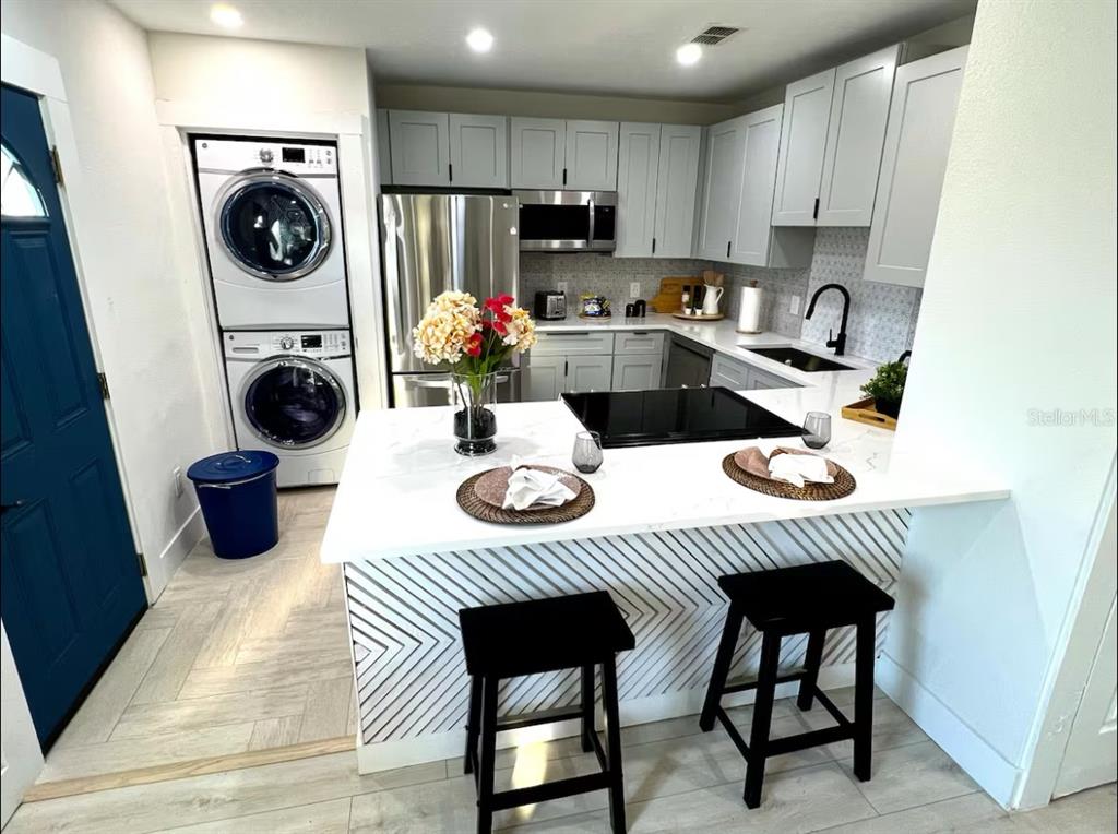 A modern kitchen features gray cabinets, white quartz countertops, stainless steel appliances, and a stacked washer-dryer — 1756 2ND STREET NE, WINTER HAVEN, FL