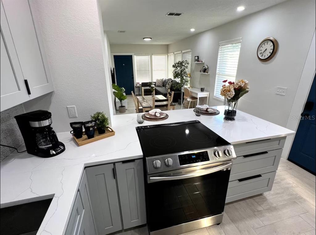 A modern kitchen features white cabinets, a quartz island with bar seating, and stacked laundry appliances — 1756 2ND STREET NE, WINTER HAVEN, FL
