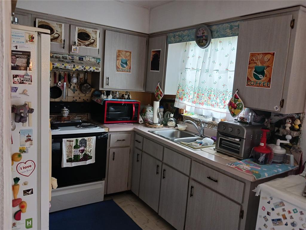 A kitchen features light wood cabinets, a black stove, a double sink, and patterned curtains — 325 ELIZABETH AVENUE, MASCOTTE, FL