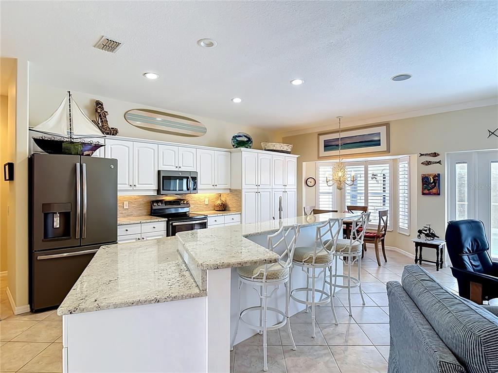 A kitchen features white cabinets, granite countertops, a large island with bar seating, and appliances — 21 RICHMOND DR, NEW SMYRNA BEACH, FL