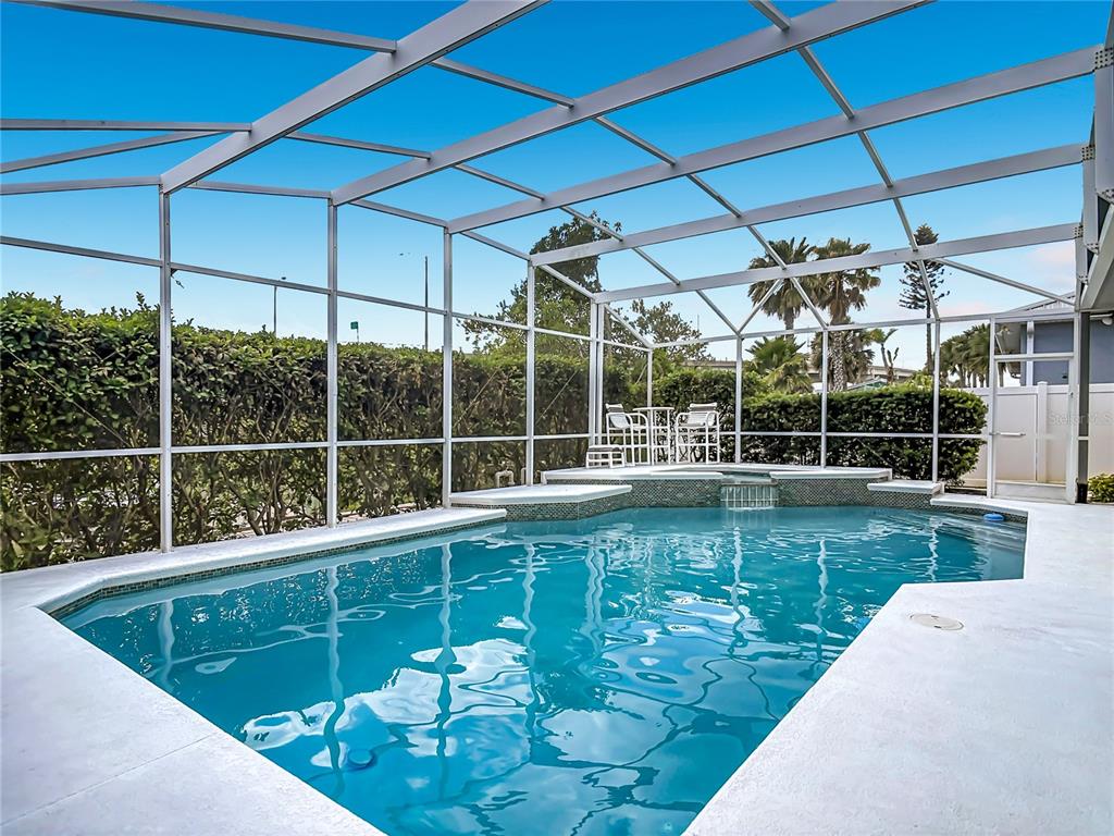 A swimming pool with a spillover spa is enclosed by a screened lanai — 21 RICHMOND DR, NEW SMYRNA BEACH, FL