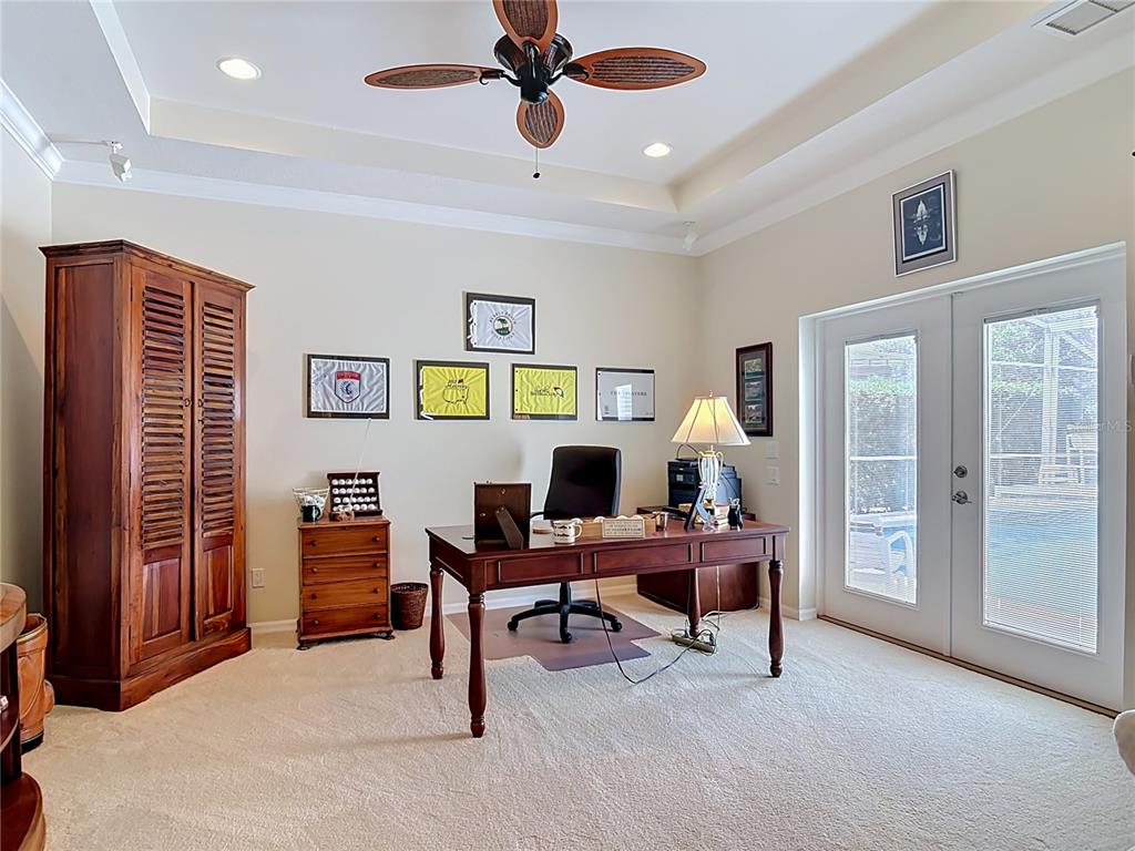 A home office features a wooden desk, a tall cabinet, and glass doors leading outside — 21 RICHMOND DR, NEW SMYRNA BEACH, FL