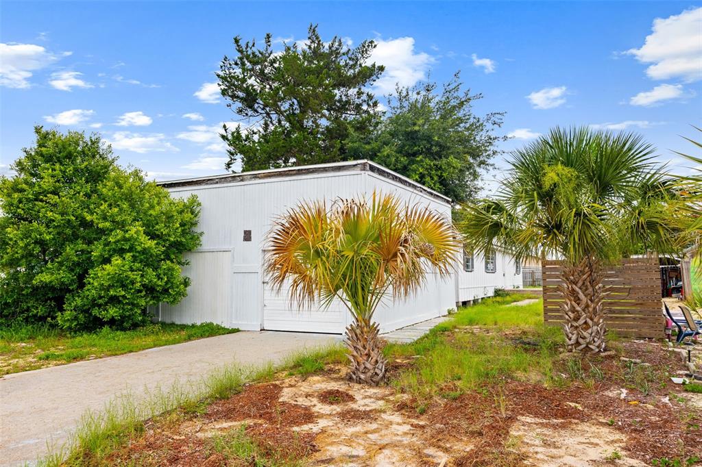A white detached garage sits on a sandy lot with palm trees and green foliage — 21316 SUNSET AVENUE, PANAMA CITY BEACH, FL
