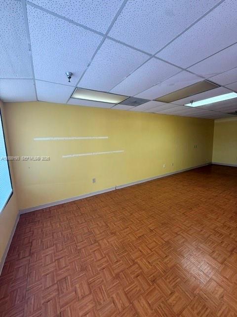 An empty office room features yellow walls, a drop ceiling, and wood-patterned flooring — 9070 Kimberly Blvd # 59, Boca Raton FL 33434, BOCA RATON, FL