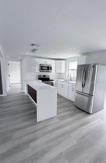 A modern kitchen features white cabinets, stainless steel appliances, and a white quartz waterfall island — 4607 PIRATE PLACE, NEW PORT RICHEY, FL