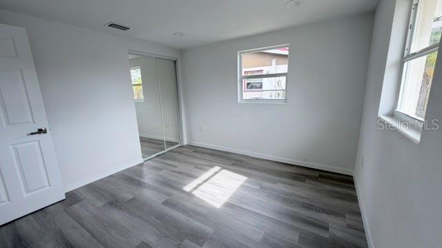 A bedroom with white walls, gray wood-look flooring, a mirrored closet, and two windows — 4607 PIRATE PLACE, NEW PORT RICHEY, FL