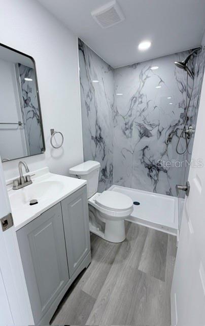 A bathroom features a gray vanity, a white toilet, and a shower with marble-patterned walls — 4607 PIRATE PLACE, NEW PORT RICHEY, FL