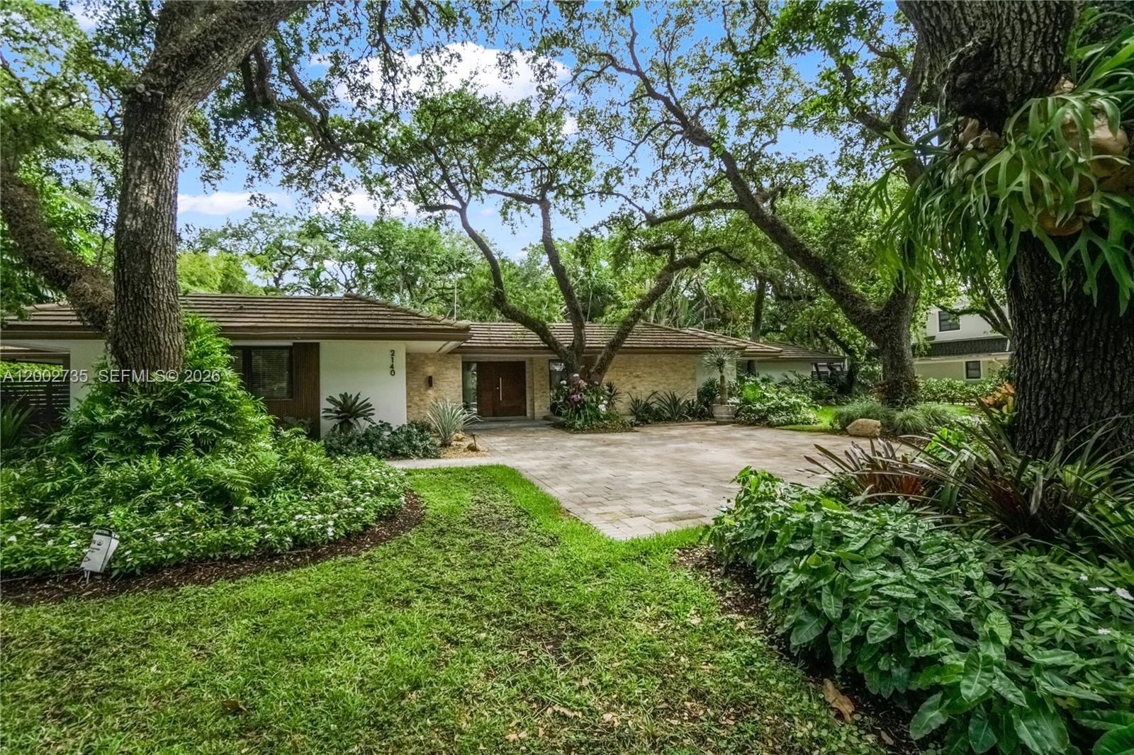 A single-story house with a stone facade and a paved driveway surrounded by large trees — 2140 NE 190th Ter, Miami FL 33179, MIAMI, FL