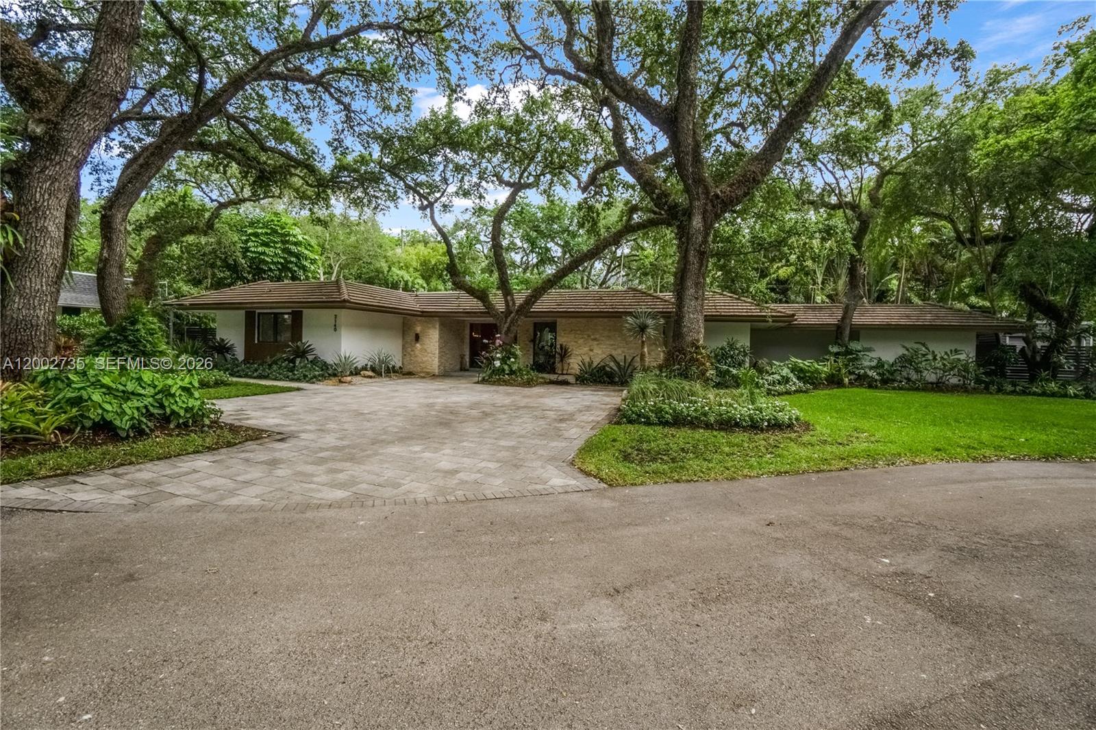 A single-story house with a paved driveway, stone accents, and large trees in the yard — 2140 NE 190th Ter, Miami FL 33179, MIAMI, FL