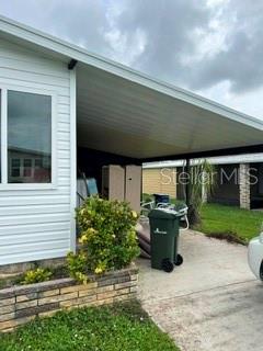 The exterior of a manufactured home features a white-sided wall, a carport, and a trash bin — 263 MARINER DRIVE, NORTH PORT, FL