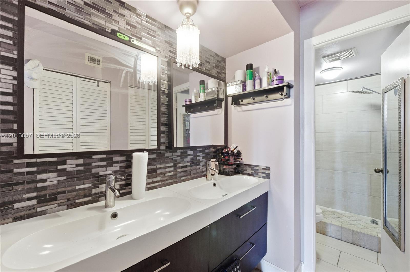 A bathroom features a double vanity with a dark cabinet, tiled backsplash, and dual mirrors — 6195 Rock Island Rd # 511, Tamarac FL 33319, TAMARAC, FL