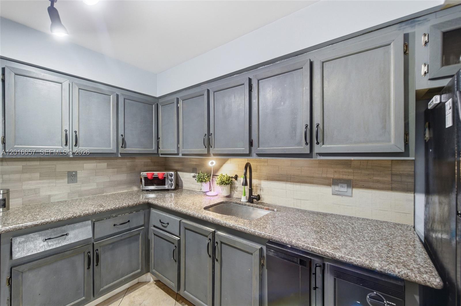A kitchen features gray cabinets, granite countertops, a tile backsplash, and a stainless steel sink — 6195 Rock Island Rd # 511, Tamarac FL 33319, TAMARAC, FL