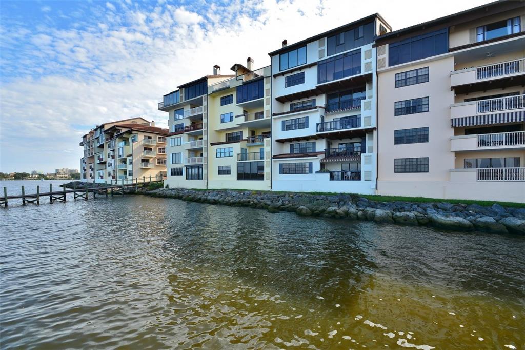 A row of multi-story waterfront apartment buildings with balconies sits along a rocky shoreline — 746 MARINA POINT DRIVE UNIT 7460, DAYTONA BEACH, FL