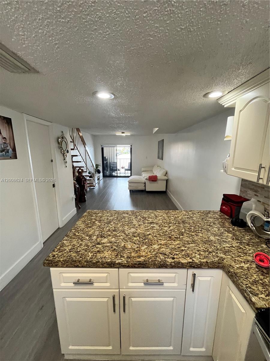 A kitchen with granite countertops overlooks a living area with stairs and a sliding door — 5580 W 26th Ct # 204, Hialeah FL 33016, HIALEAH, FL