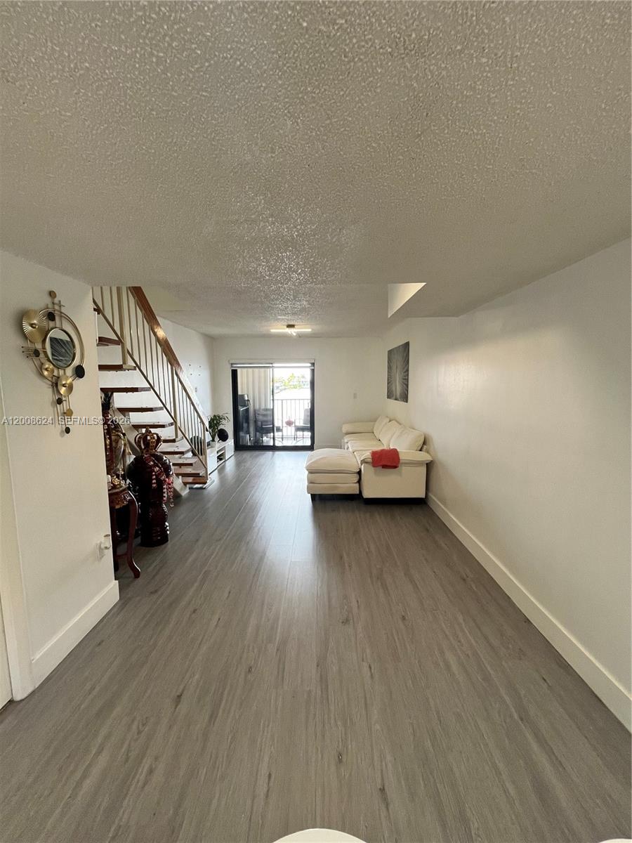 A living room features wood-look flooring, a white sectional sofa, and a staircase with railings — 5580 W 26th Ct # 204, Hialeah FL 33016, HIALEAH, FL