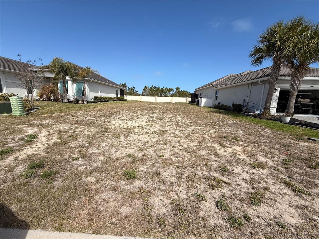 A vacant residential lot sits between two houses under a clear blue sky — 6 DEL PALMA DRIVE, PALM COAST, FL