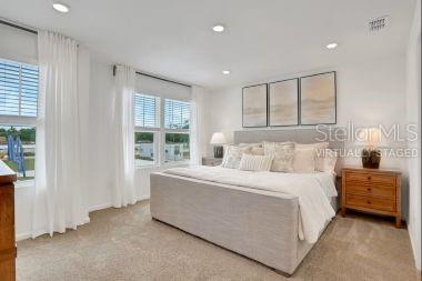 A bedroom features a large bed, a wooden nightstand, and windows with white curtains — 7634 COMMANDER LANE, JACKSONVILLE, FL
