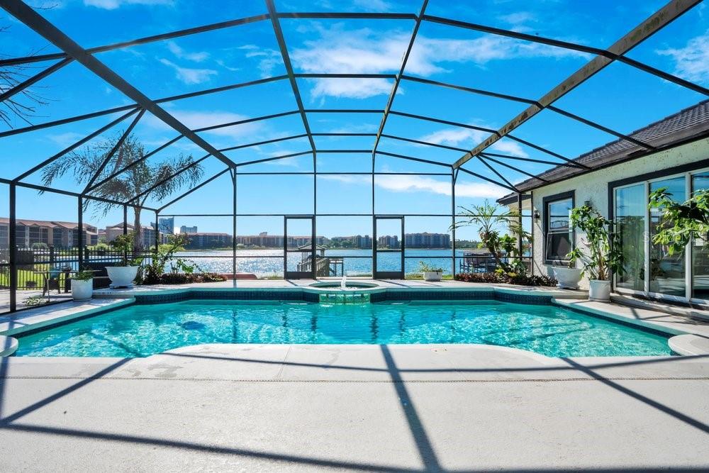 A screened-in swimming pool and spa overlook a lake with apartment buildings in the distance — 10094 BRANDON CIRCLE, ORLANDO, FL