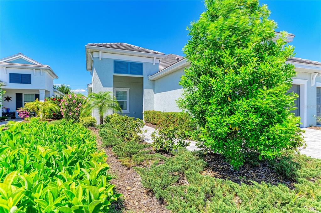 A light-colored house exterior features a covered entryway, a walkway, and manicured landscaping — 12807 SEASONG TERRACE, BRADENTON, FL